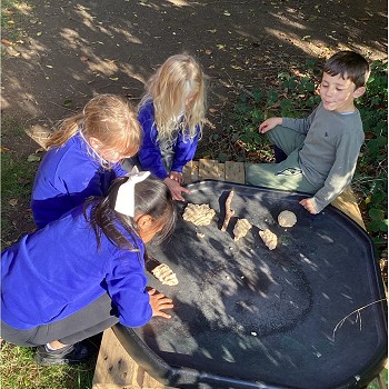 Children playing on an outdoor water table in a wooded area.